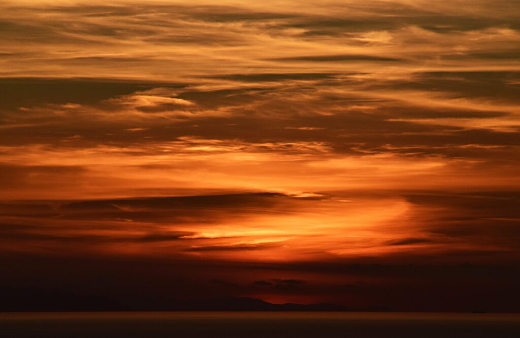 Breathtaking sunset wallpaper with swirling orange clouds and warm golden glow over calm sea
