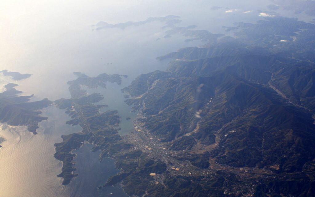Top view of rugged mountains and calm coastline with soft clouds and misty atmosphere wallpaper
