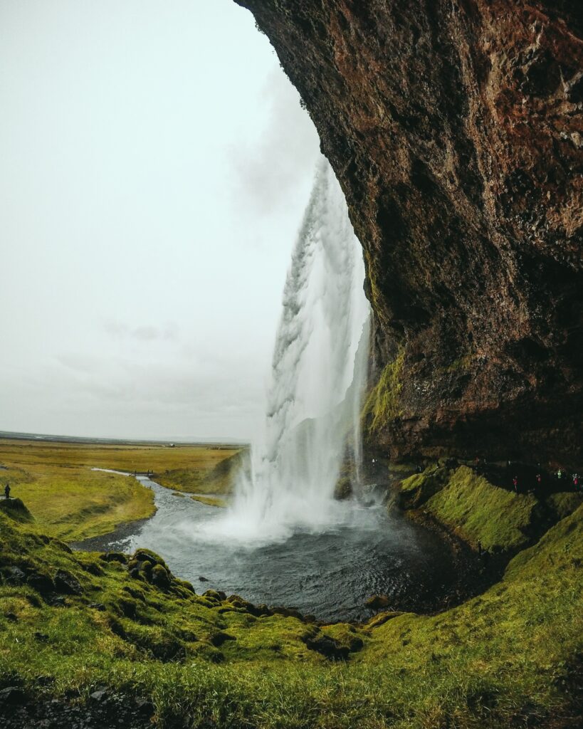 Waterfall cascading down rocky cliff into river with lush moss and overcast sky wallpaper background