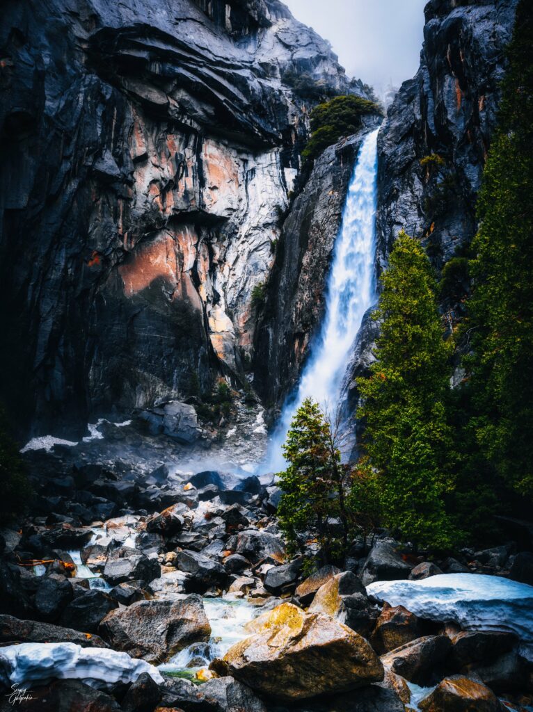 Waterfall cascading over rocky cliffs surrounded by lush green trees in vibrant natural landscape Wallpaper