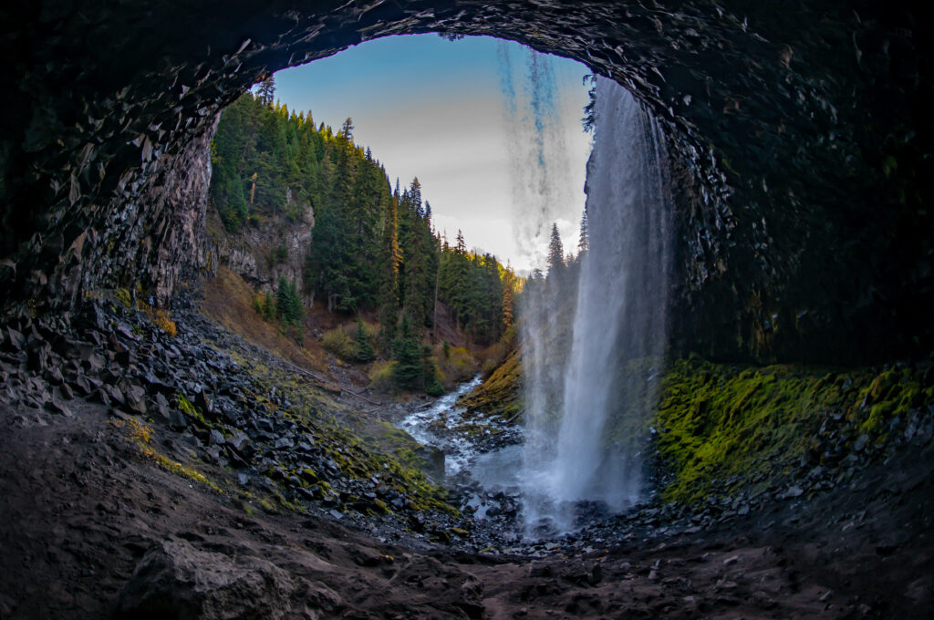 Waterfall cascading through natural stone arch surrounded by rugged rocks and lush green forest Wallpaper