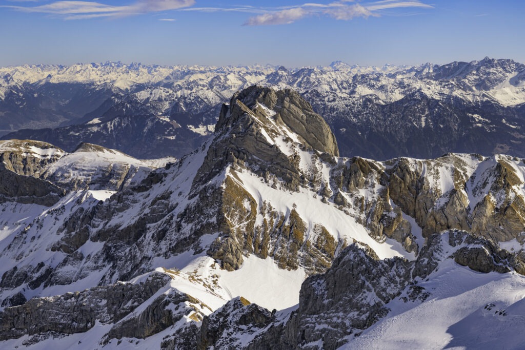 Snowy mountain landscape with rugged rocky slopes and distant alpine peaks under clear sky Wallpaper