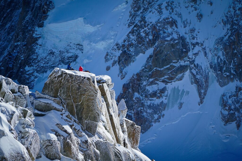 Tourists in colorful jackets on snow-covered rocks with dramatic icy cliffs and mountain views Wallpaper