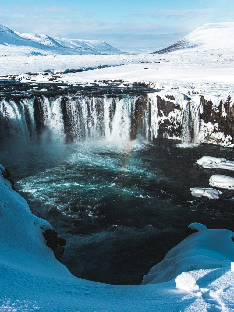 Aerial view of a powerful waterfall in a snowy winter landscape with distant blue mountains wallpaper