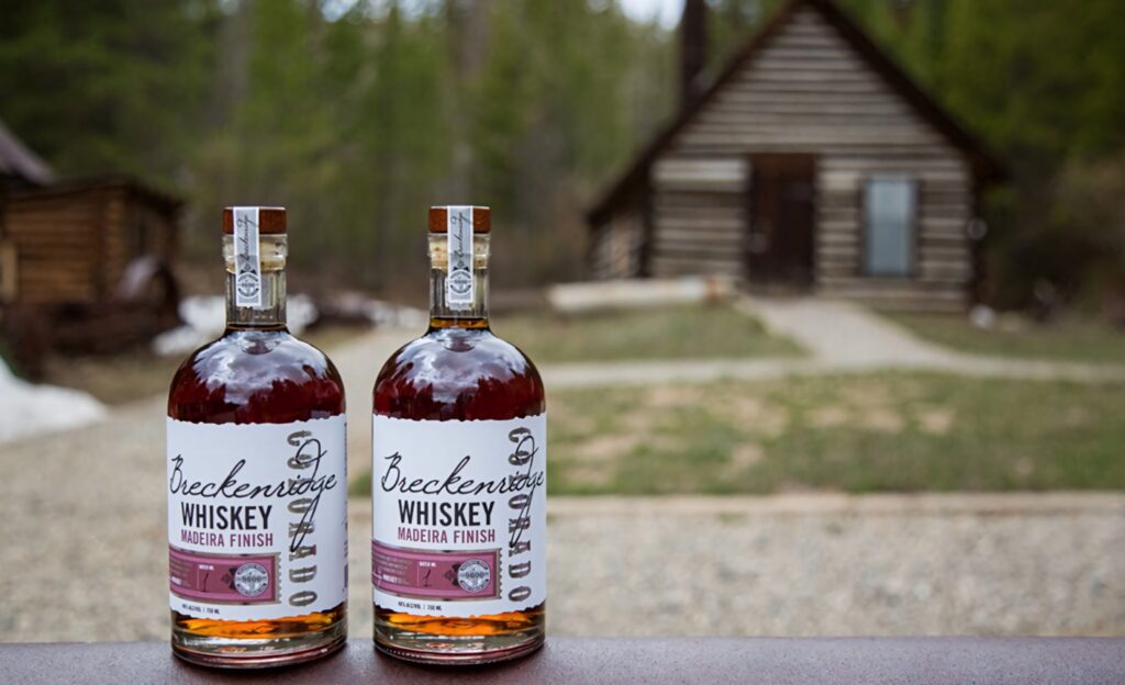 Breckenridge Distillery Whiskey Madeira Finish bottles outdoors with rustic cabins and green trees Wallpaper