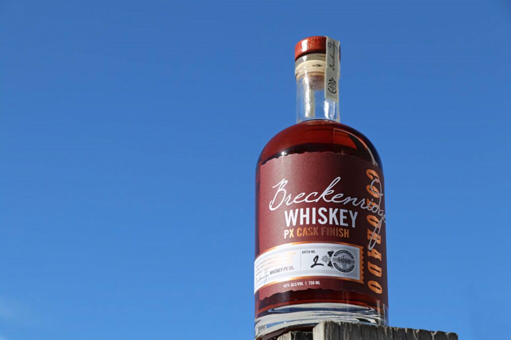 Breckenridge Distillery PX Cask Finish whiskey bottle with amber color against blue sky wallpaper