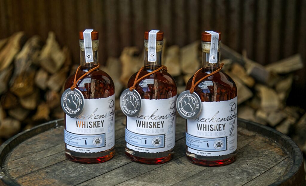 Breckenridge Distillery Powder Hound Bourbon bottles on wooden barrel rustic mountain background Wallpaper