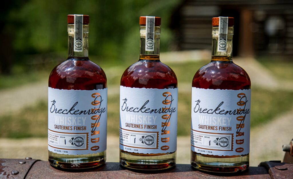 Three Breckenridge Whiskey Sauternes Finish bottles outdoors amber glow premium craft spirits Wallpaper