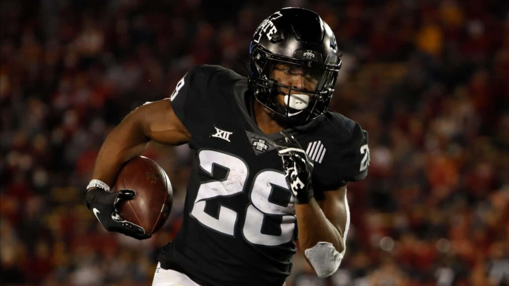 Breece Hall running back mid-run football action wallpaper stadium background athletic energy