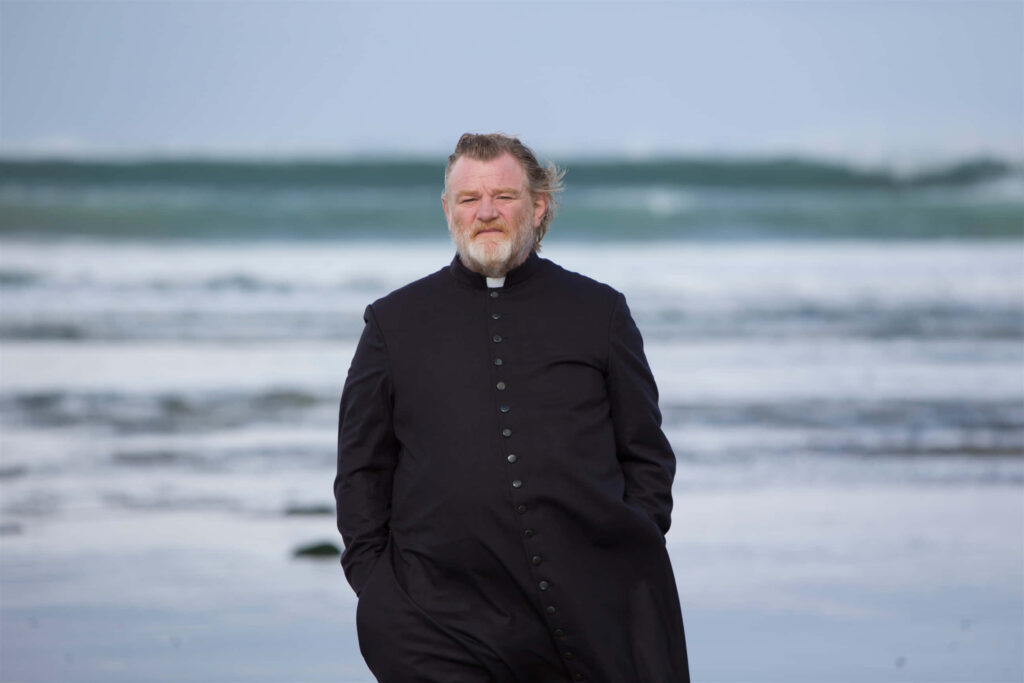 Brendan Gleeson in black cassock on serene beach with ocean waves cinematic wallpaper background