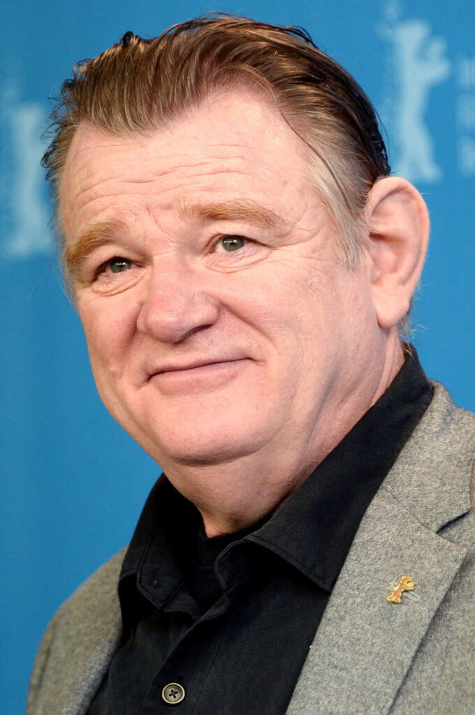 Brendan Gleeson close-up portrait on blue background showcasing charming expression and style Wallpaper