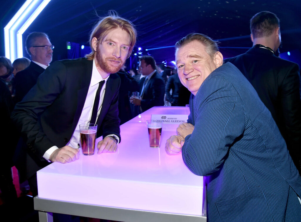 Brendan and Domhnall Gleeson in elegant suits at blue-lit modern event warm father son moment wallpaper