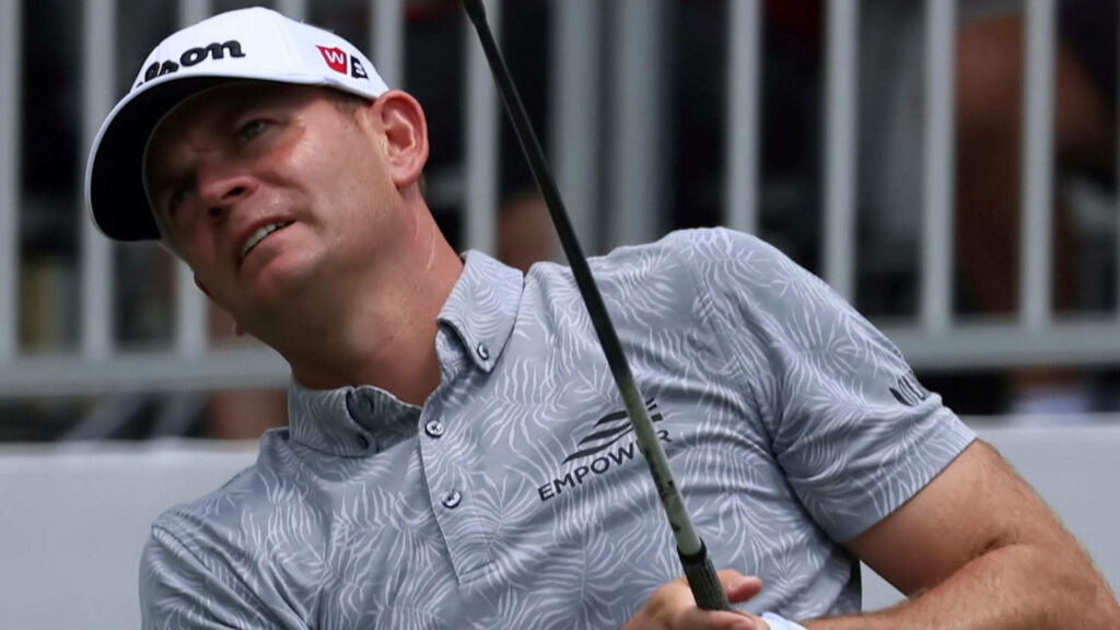 Professional golfer Brendan Steele mid-swing leaning back in gray shirt white cap stadium background wallpaper