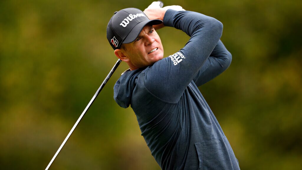 Brendan Steele mid-swing wearing navy jacket golfing on blurred green background wallpaper