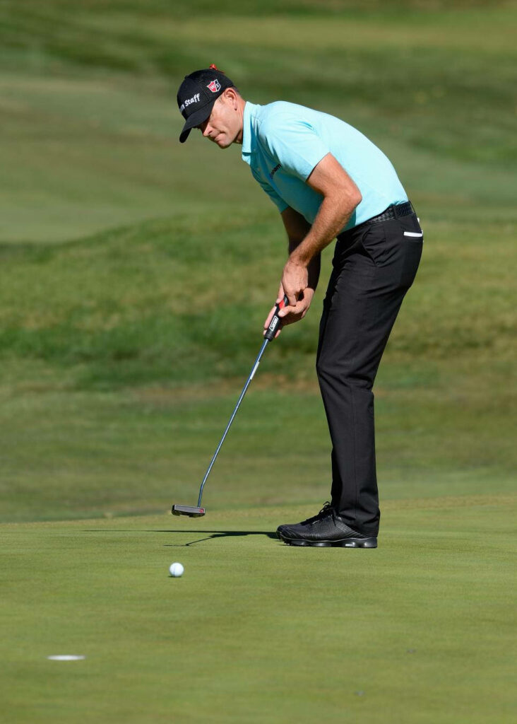 Pro golfer Brendan Steele focused on precision putt inches from hole on sunlit golf green Wallpaper