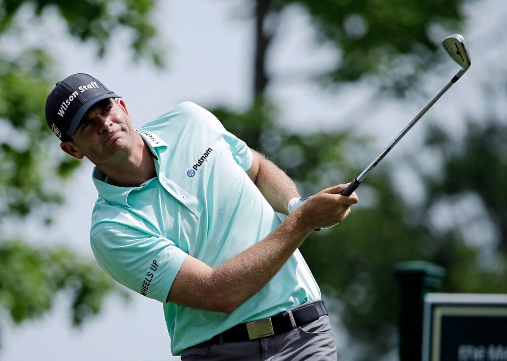 Brendan Steele mid-swing golf wallpaper teal polo black cap green course clear skies background