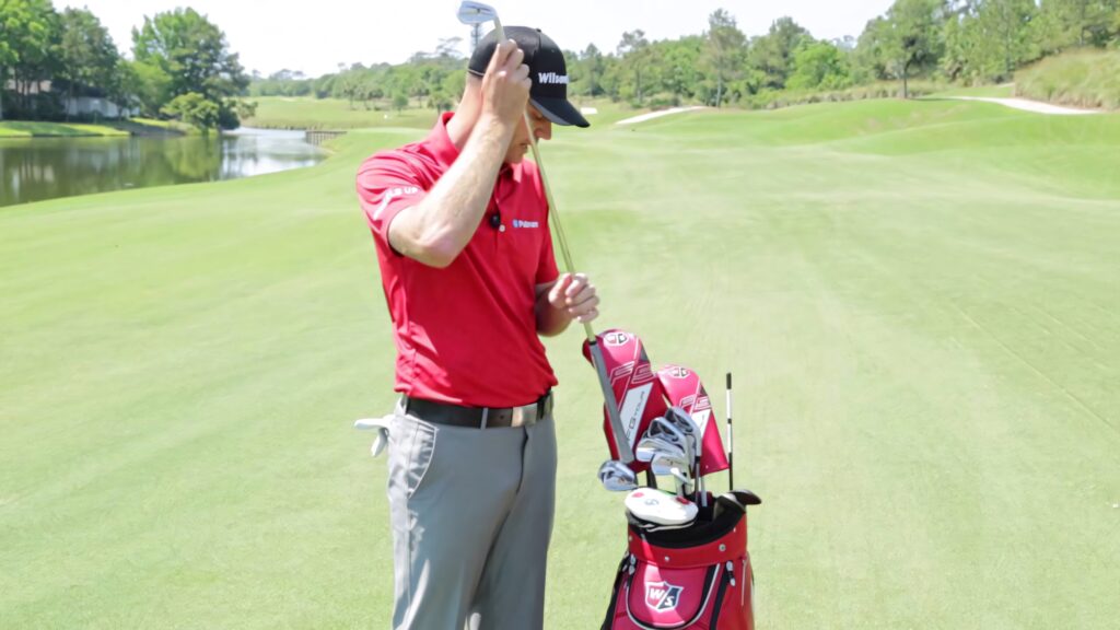 Brendan Steele selecting golf club on lush green course with red Wilson bag in bright daylight Wallpaper