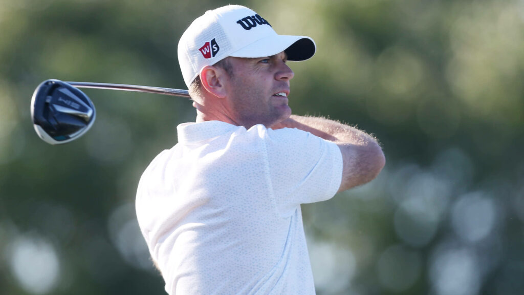 Brendan Steele mid-swing in white shirt and cap focused on golf shot against green background Wallpaper