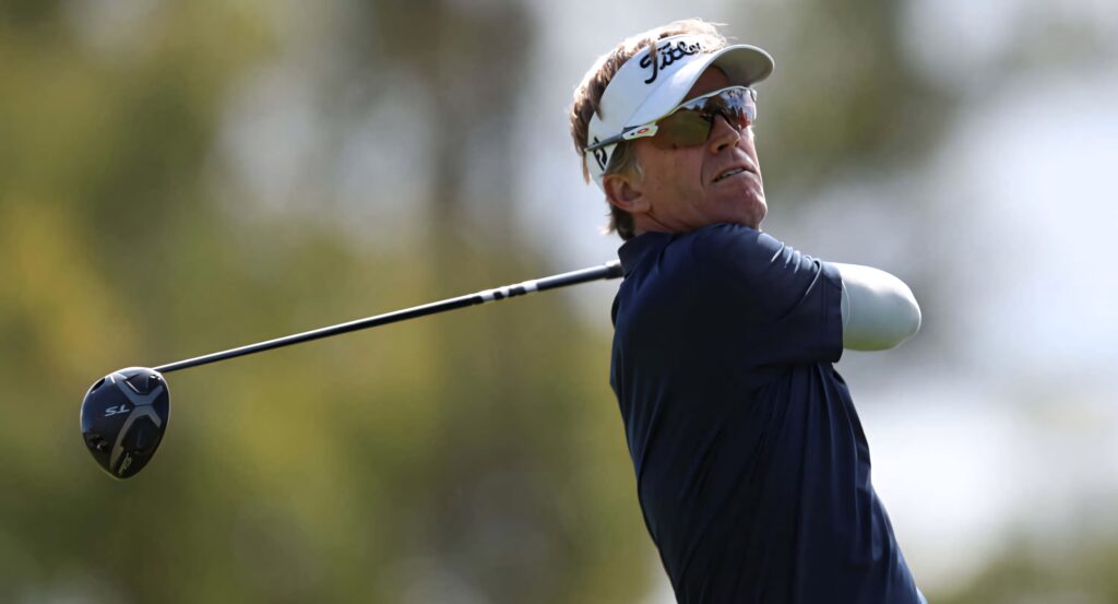 Brett Quigley focused golf swing action shot in classic attire with white visor on blurred background Wallpaper