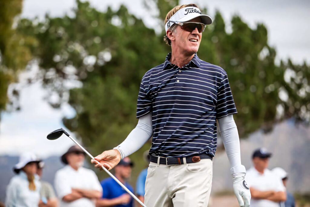 Brett Quigley golfer in striped polo visor sunglasses on golf course with blurred spectators wallpaper