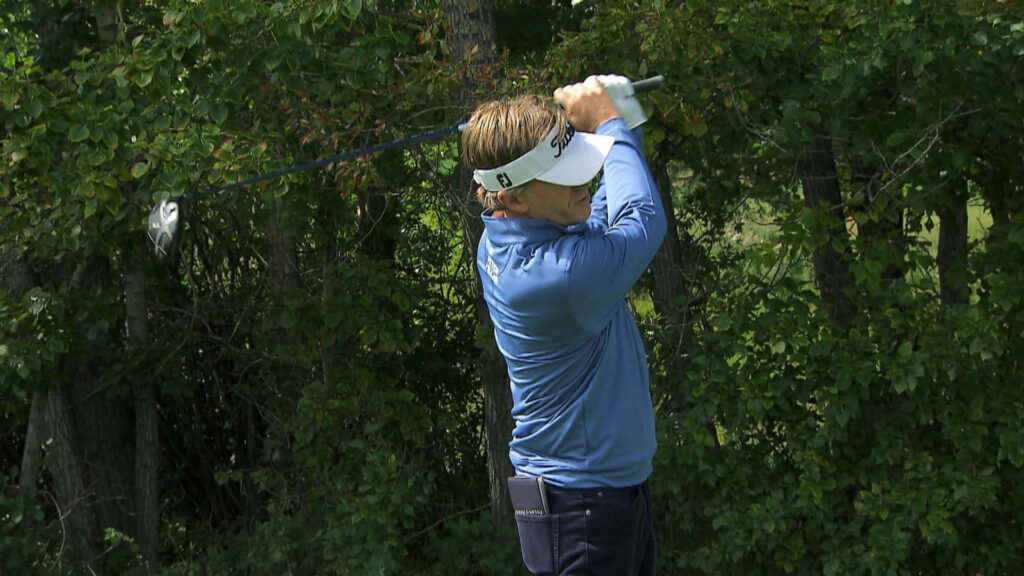 Brett Quigley mid-swing golf shot with vibrant green leafy trees golf course wallpaper background