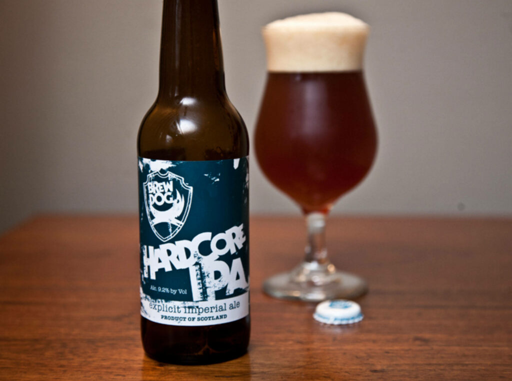 Close-up BrewDog Hardcore IPA bottle with blue label and amber beer in tulip glass on table Wallpaper