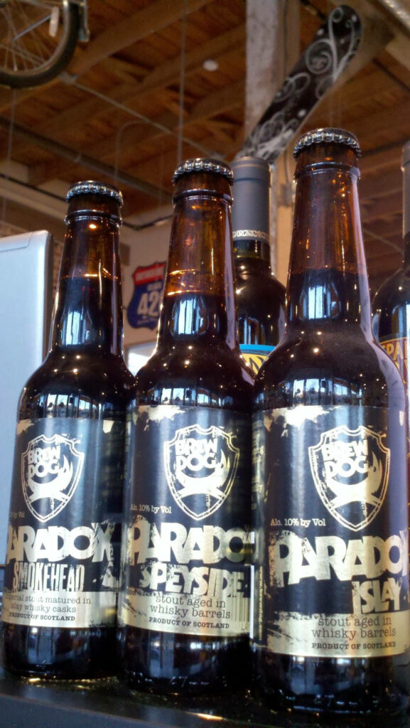 Three BrewDog Paradox Islay stout bottles with dark glass and gold labels on industrial background Wallpaper