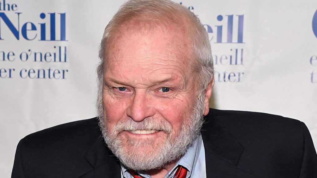 Brian Dennehy close-up portrait with smile grey beard sharp attire white and blue background wallpaper