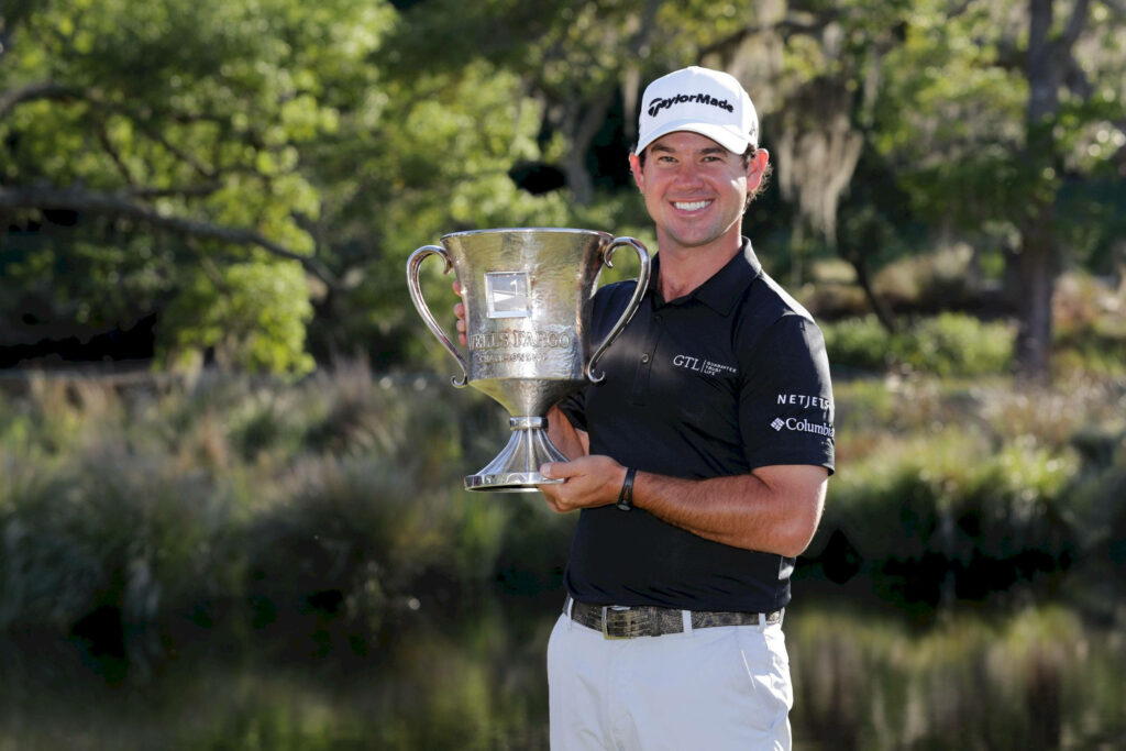 Brian Harman celebrating golf victory holding silver trophy on sunny lush green course wallpaper