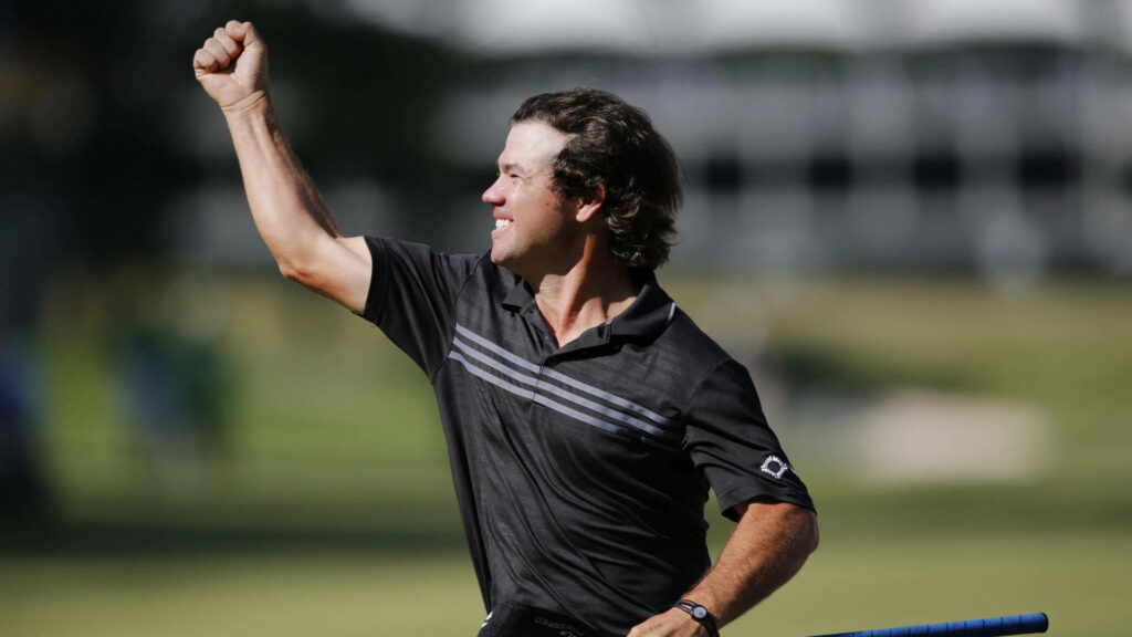 Brian Harman celebrating with fist raised on sunlit golf course vibrant victory wallpaper background