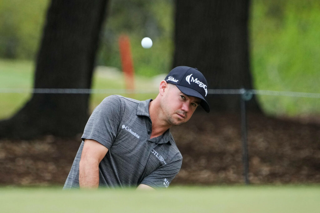 Professional golfer Brian Harman mid-swing on lush green golf course with intense focus and motion blur Wallpaper