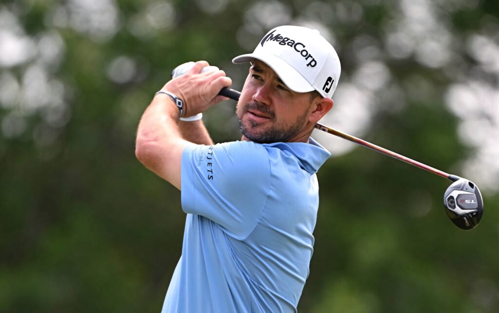Brian Harman golf swing action in light blue shirt white cap with green foliage background wallpaper
