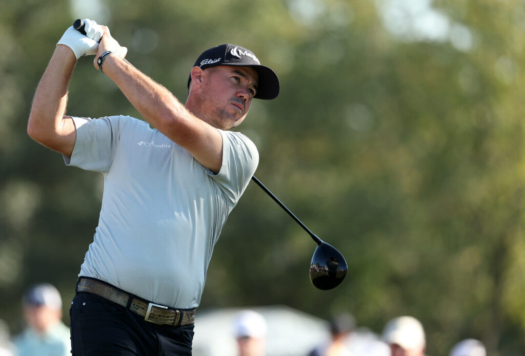 Brian Harman mid golf swing wearing gray shirt and black cap with green golf course background Wallpaper