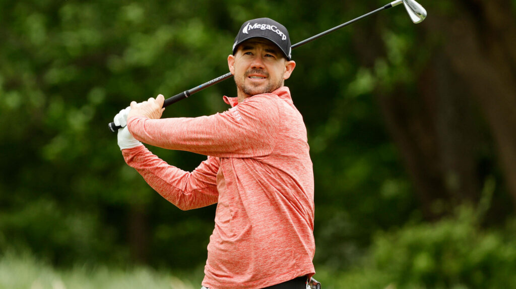 Brian Harman mid swing golf wallpaper red shirt black cap lush green golf course background