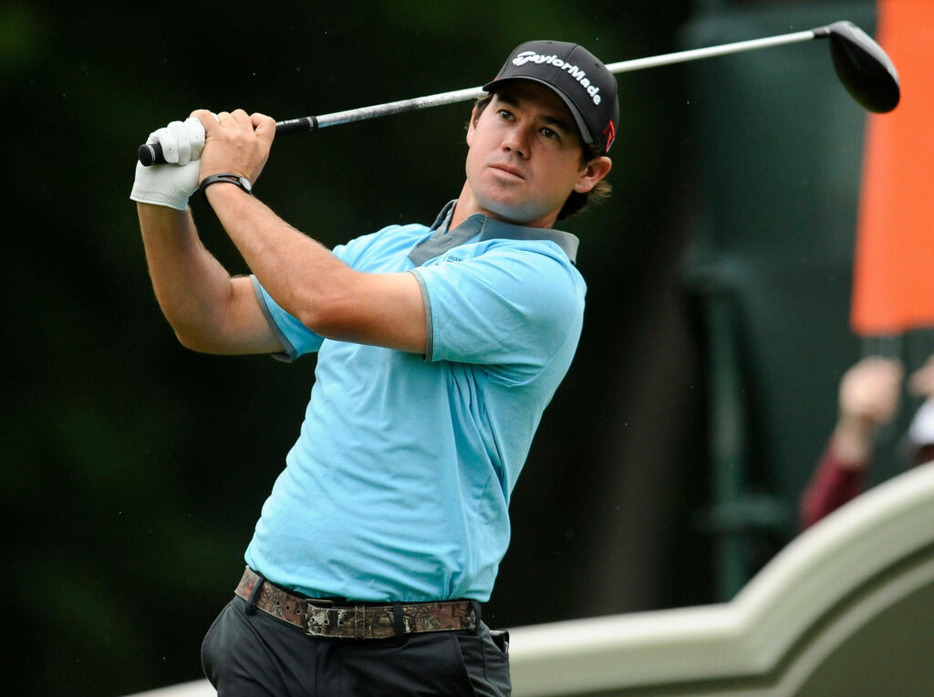 Brian Harman mid-swing golf tee wallpaper in light blue polo black Taylormade cap green background