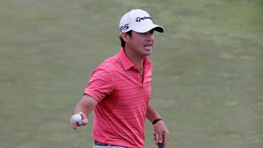Brian Harman golf wallpaper showing pro golfer in red shirt holding golf ball and club on course