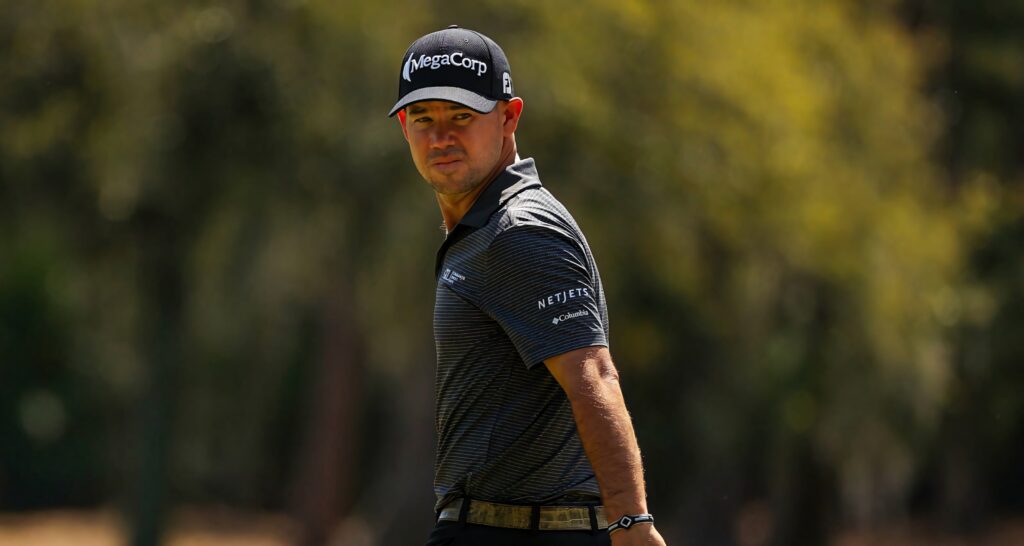 Brian Harman golf portrait glancing over shoulder in MegaCorp cap on blurred golf course background Wallpaper
