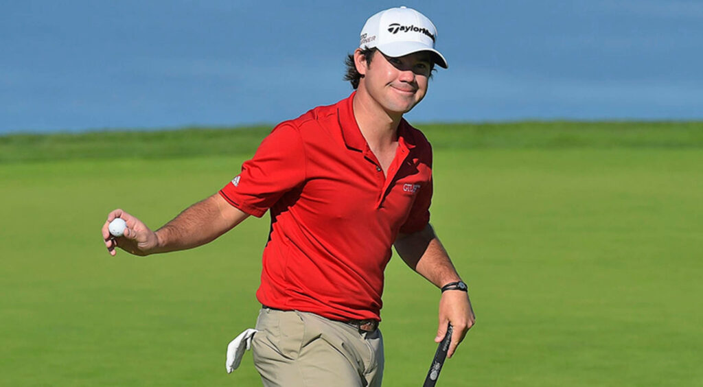 Brian Harman in red polo on green golf course holding putter and ball confident golfer pose Wallpaper