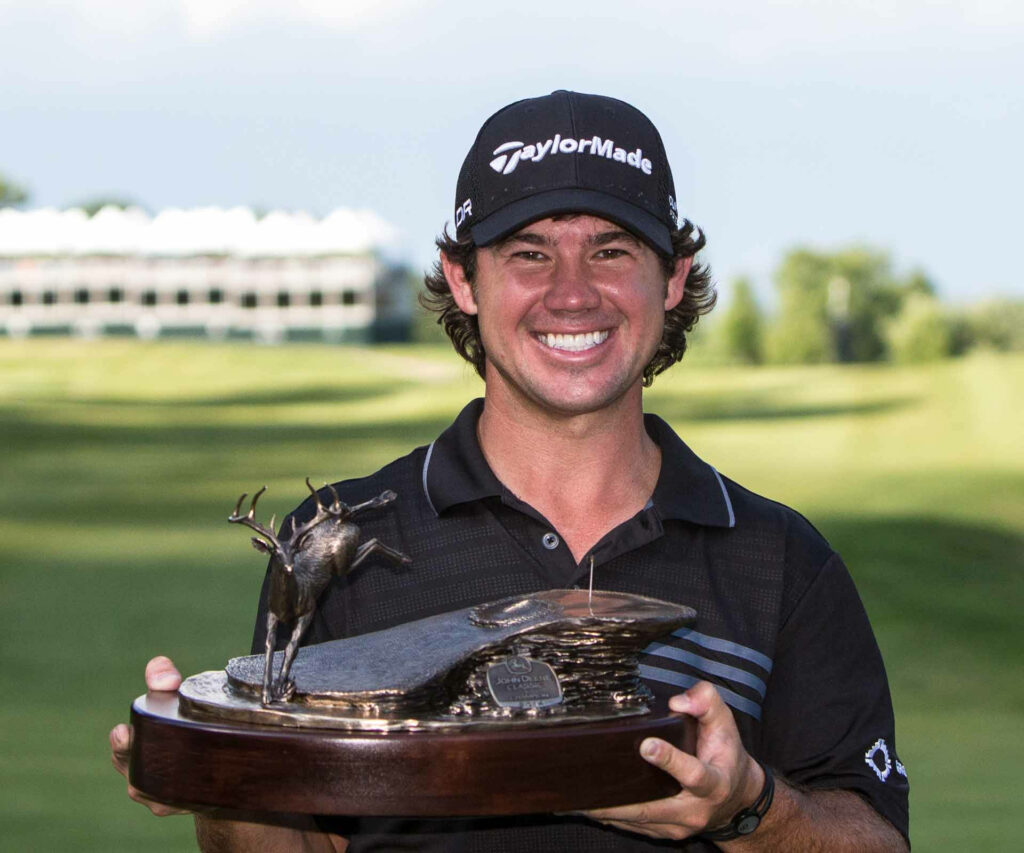 Brian Harman smiling proudly holding tournament trophy on lush green golf course background Wallpaper