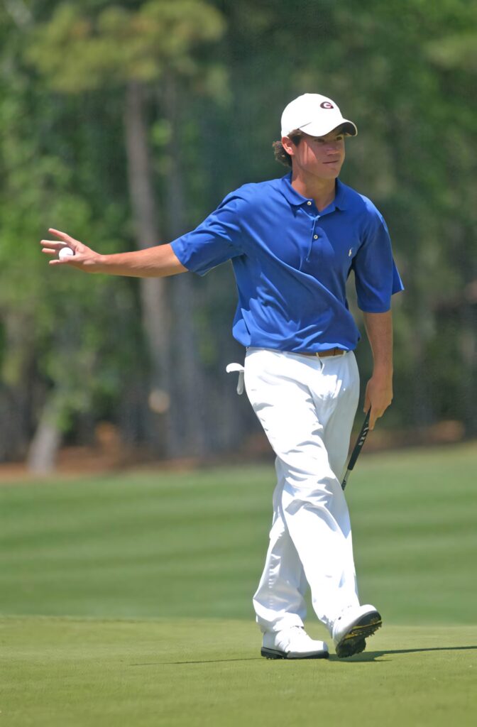 Brian Harman waving on green golf course wearing blue polo and white pants holding putter and ball Wallpaper