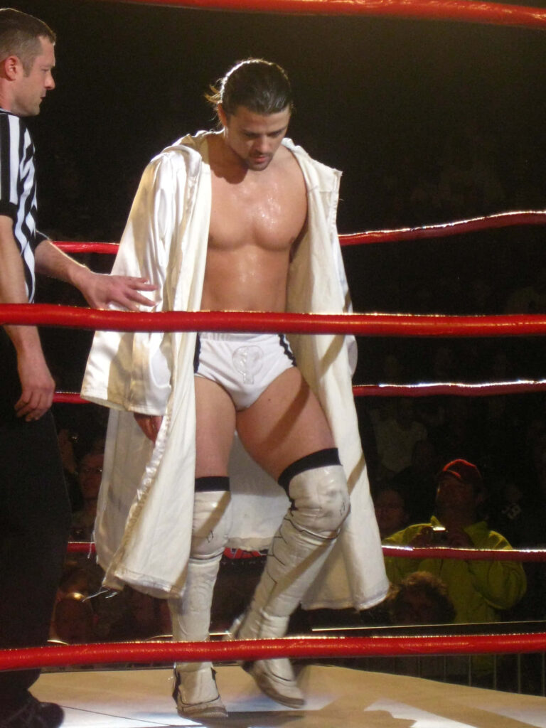 Brian Kendrick in white robe in wrestling ring with red ropes dramatic lighting intense sports wallpaper