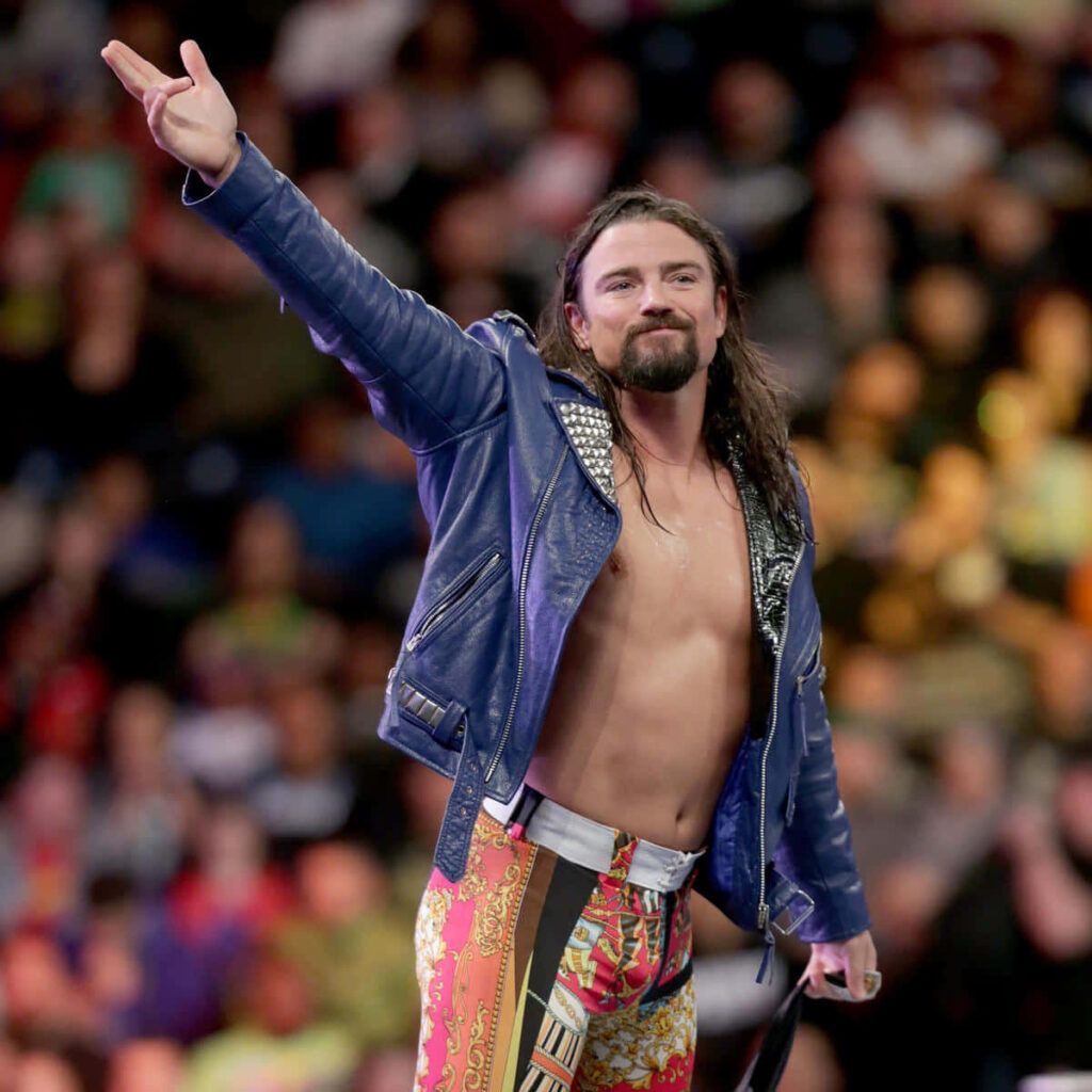 Brian Kendrick confident wrestling pose in vibrant arena wearing blue studded jacket and tights Wallpaper