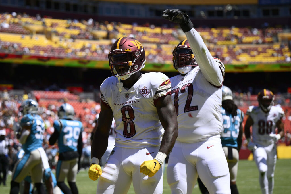 Brian Robinson Jr celebrating key play with teammate in Washington Commanders burgundy gold uniform Wallpaper