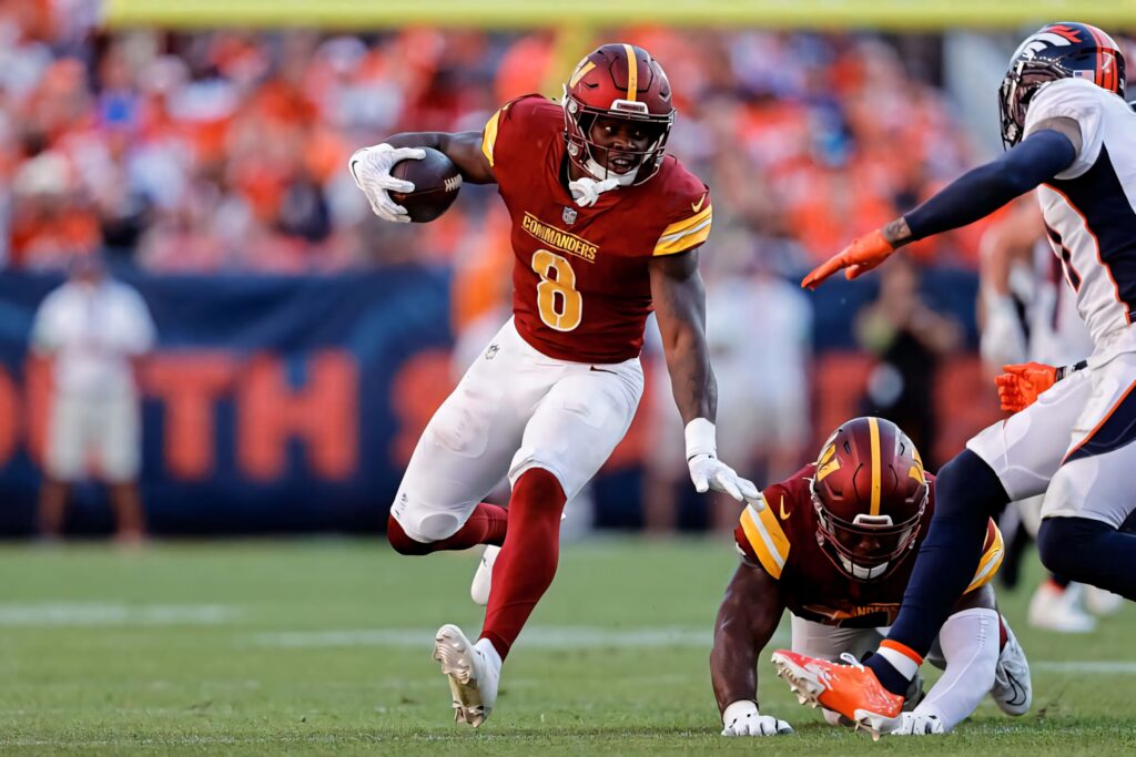 Brian Robinson Jr. Commanders evading tackle in burgundy and gold uniform on football field wallpaper