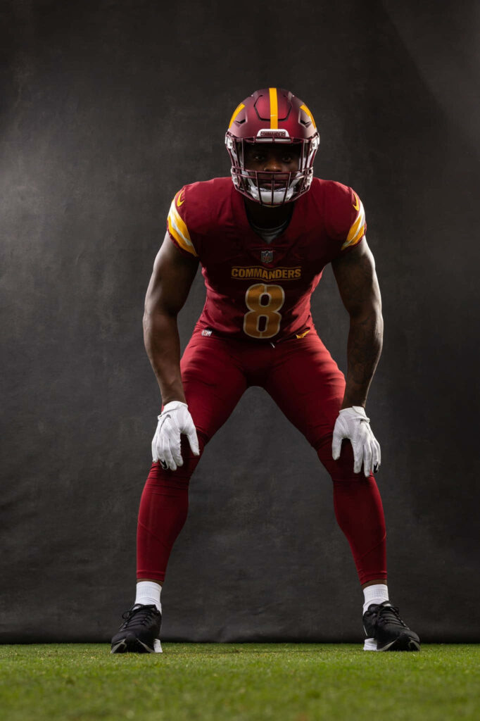 Brian Robinson Jr Commanders football player in ready stance vibrant red gold background wallpaper