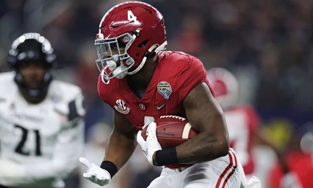 Brian Robinson Jr running with ball in red Alabama jersey during intense football game action wallpaper
