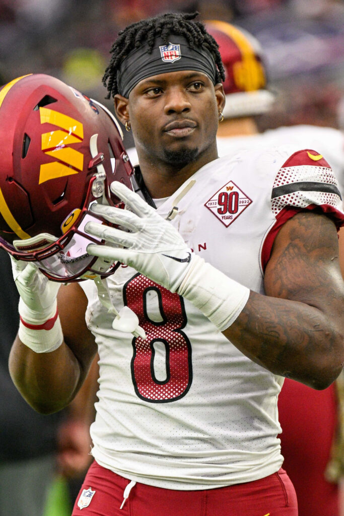 Brian Robinson Jr. in Washington Commanders uniform holding helmet on vibrant stadium field Wallpaper