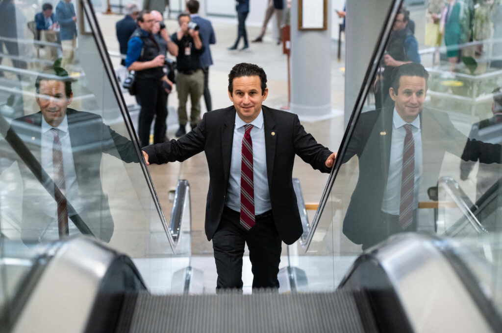 Brian Schatz climbing modern glass escalator in sharp suit showcasing leadership and progress Wallpaper
