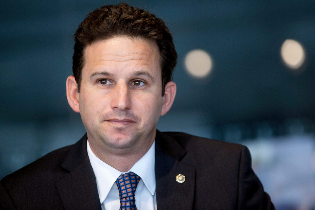 Brian Schatz formal portrait navy suit patterned tie contemplative expression dark background wallpaper