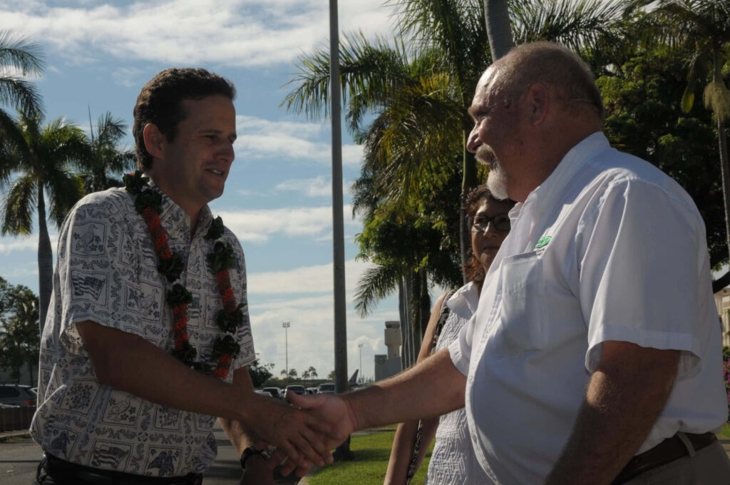Brian Schatz shaking hands outdoors with palm trees and clear skies vibrant community wallpaper background